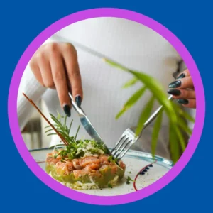 A hands use a knife and fork to cut into salmon.