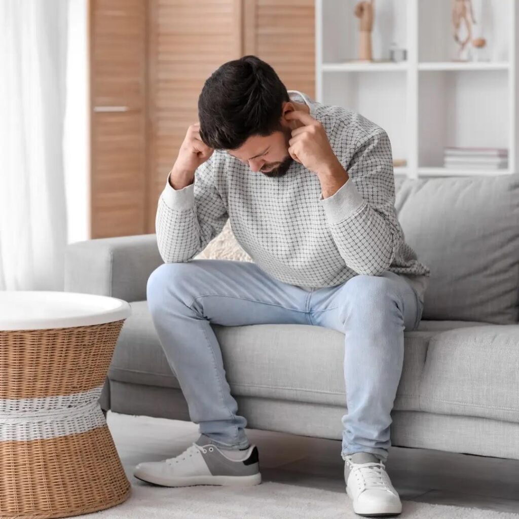 An uncomfortable man holds his hands over his ears.
