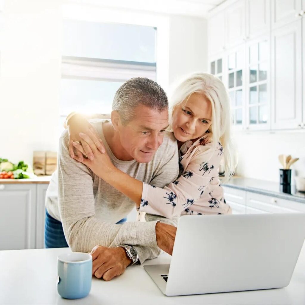 An older couple looks at their laptop together.