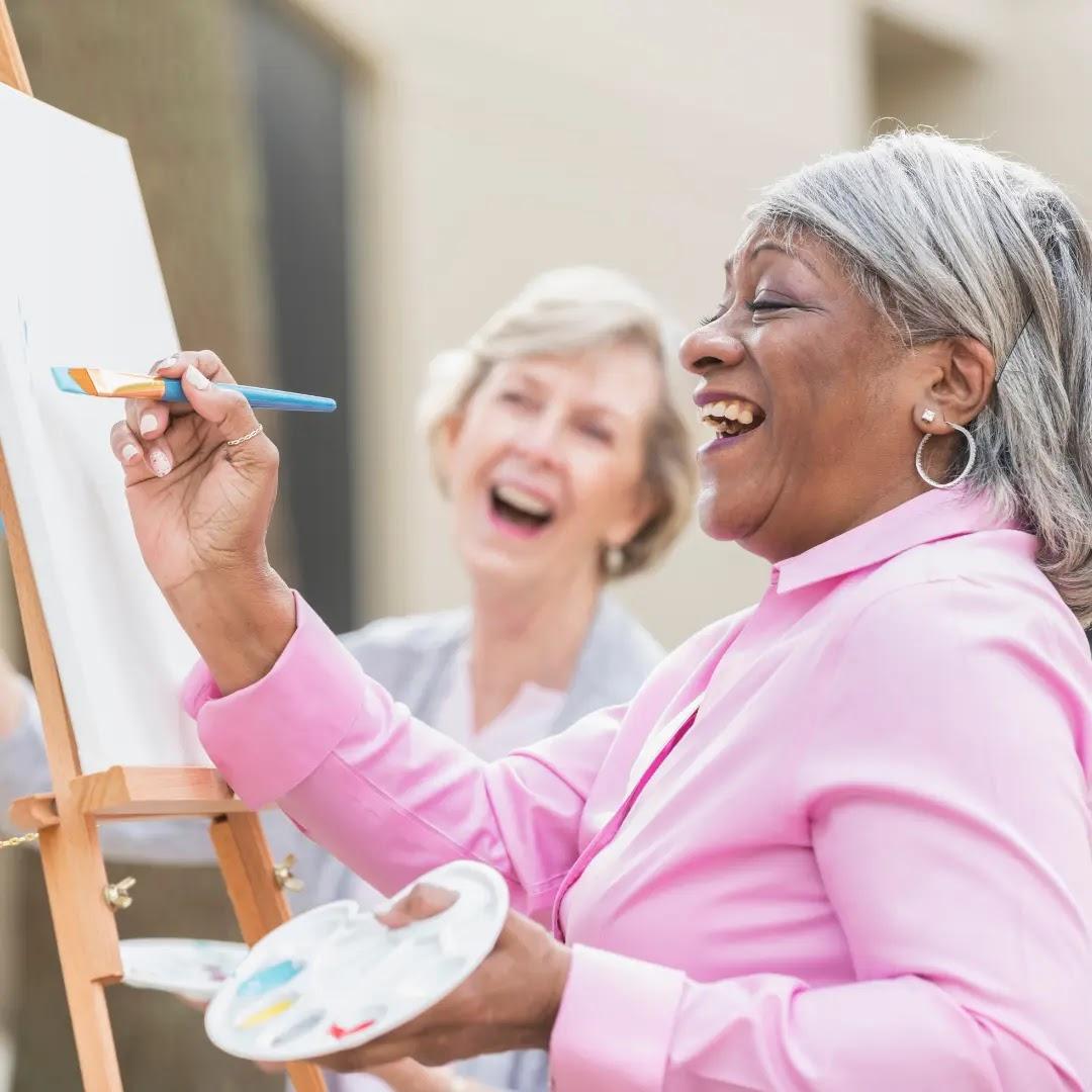 Two older women paint happily outside.