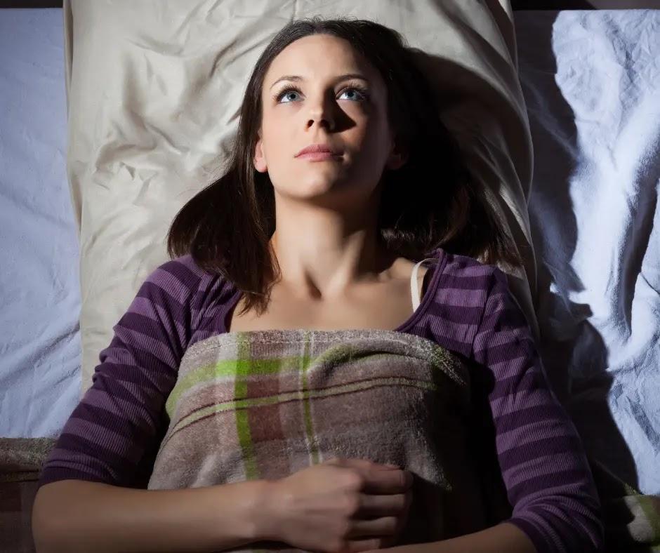 A woman lies in bed and stares at the ceiling.