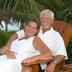 A smiling older couple poses together on a tropical vacation.