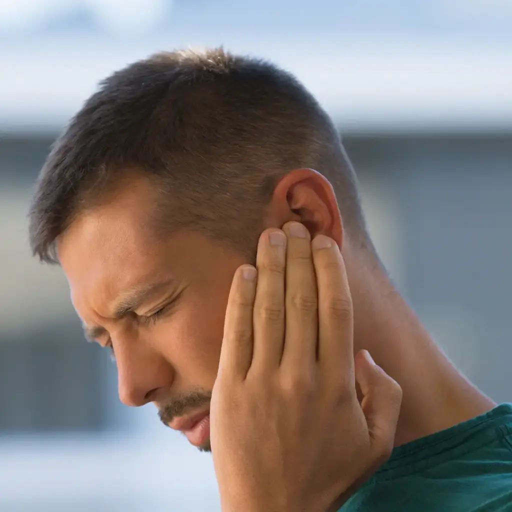 A man grimaces and holds his ear.