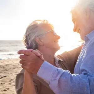 A smiling older couple dances together on a beach.