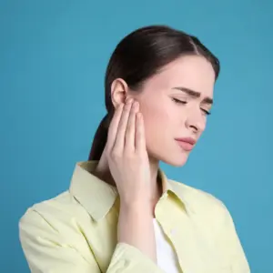 A woman holds her hearing aid and winces in discomfort. 