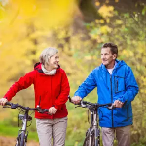 An older couple pushes their bikes up a hill. 