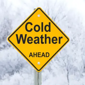A yellow caution sign says, “Cold Weather Ahead,” and stands in the snow.