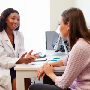 An audiologist talks to a patient at her desk. 