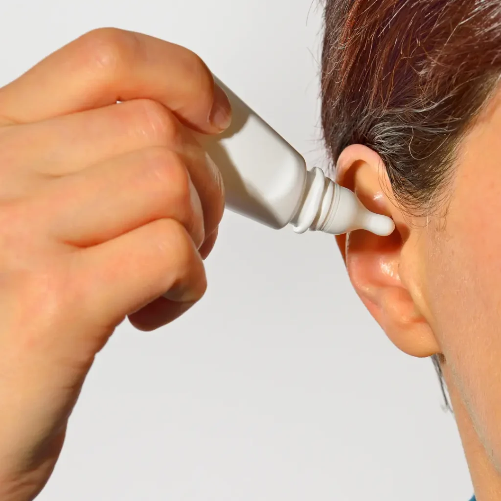 A man puts ear drops into his ear for ear wax removal.