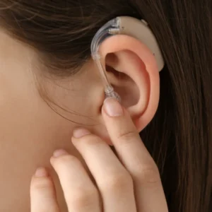 A finger holds a hearing aid receiver in an ear.