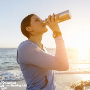 A woman drinks from a bottle of water at the beach.