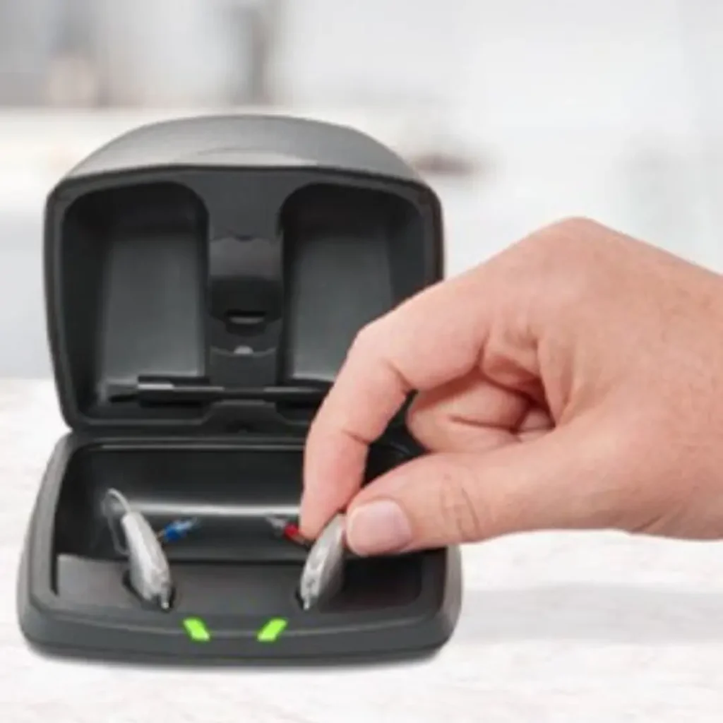 A hand places hearing aids into their charging case.