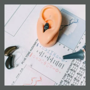 Hearing aids, an otoscope, and a model ear sit on top of a hearing test. 