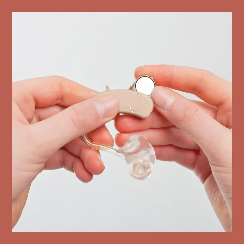 Hands put a battery into a hearing aid.