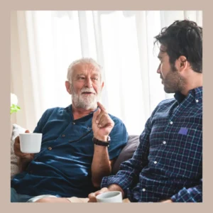 Two men sit on a couch talking to each other. 
