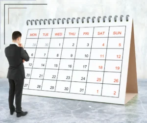 A man stands before a giant desk calendar page showing a month.