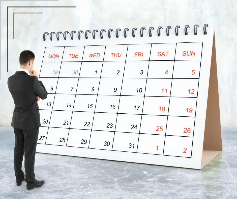 A man stands before a giant desk calendar page showing a month.