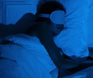A woman lies in bed wearing an eye mask. 