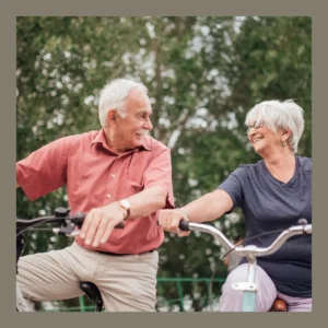 An older couple smiles at each other as they pause on a bike ride. 