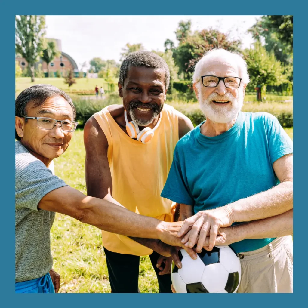 Three older men smile and hold a soccer ball while playing outside.