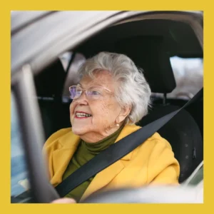 An older smiles as she drives her car. 