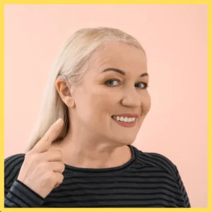 A woman smiles as she points to her hearing aid. 