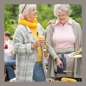 Two older woman talk together at an outdoor barbecue. 