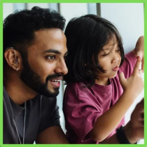 A father wearing a hearing aid helps his young daughter.