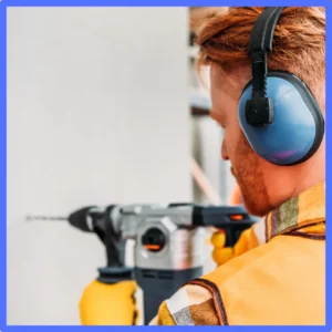 A man drills into a wall while wearing hearing protection.