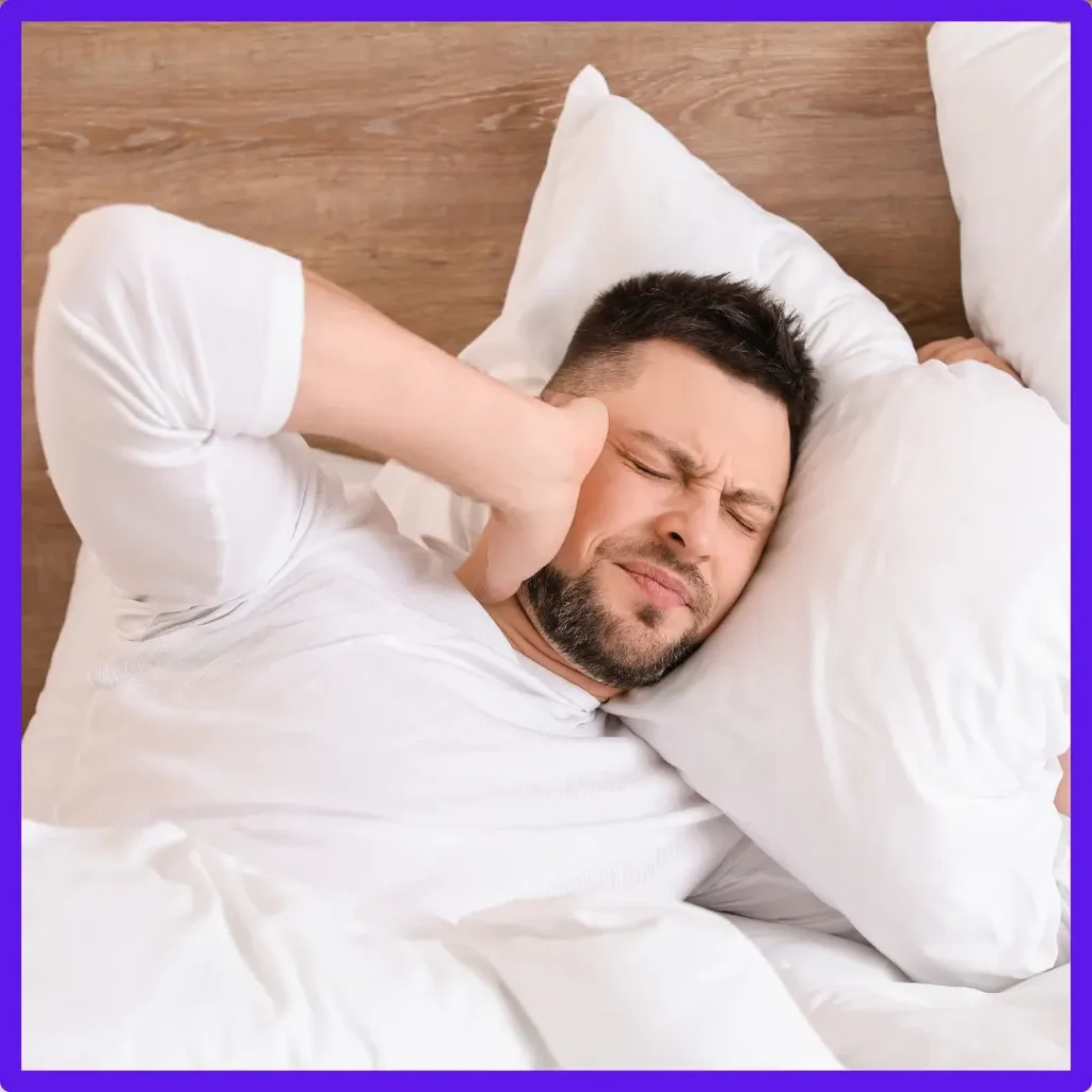 A man grimaces and holds his ear in bed.