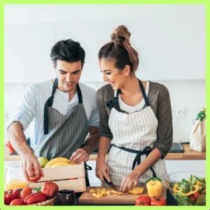 A couple cuts up fruits and vegetables in their kitchen. 