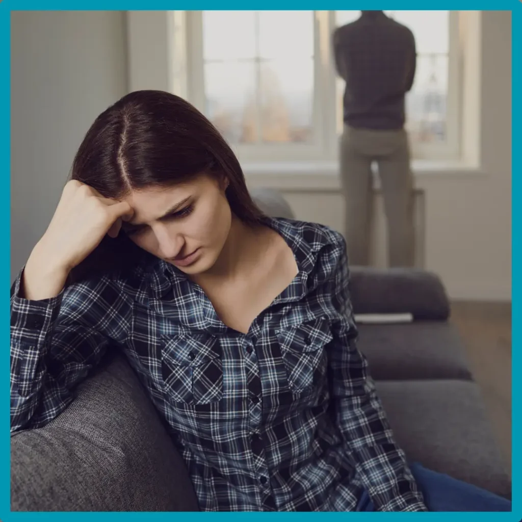 A woman looks sad as her partner stares out the window.