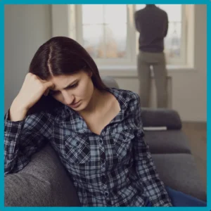 A woman looks sad as her partner stares out the window.