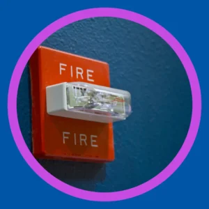 A fire alarm with a light sits on a blue wall. 