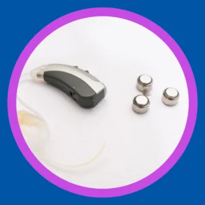 Disposable hearing aid batteries sit next to a hearing aid. 