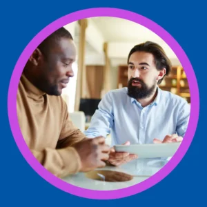 Two men talk at a table.