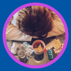 A sick woman puts her head down next to tea and medicine.