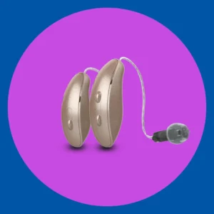 A pair of hearing aids sit on a purple background. 