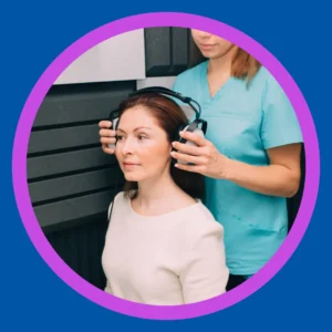 An audiologist places headphones a woman's head. 
