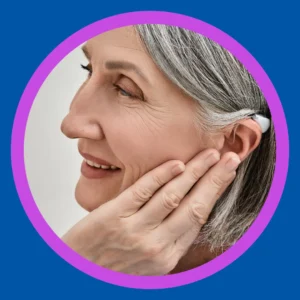 A woman smiles and holds her hearing aids. 